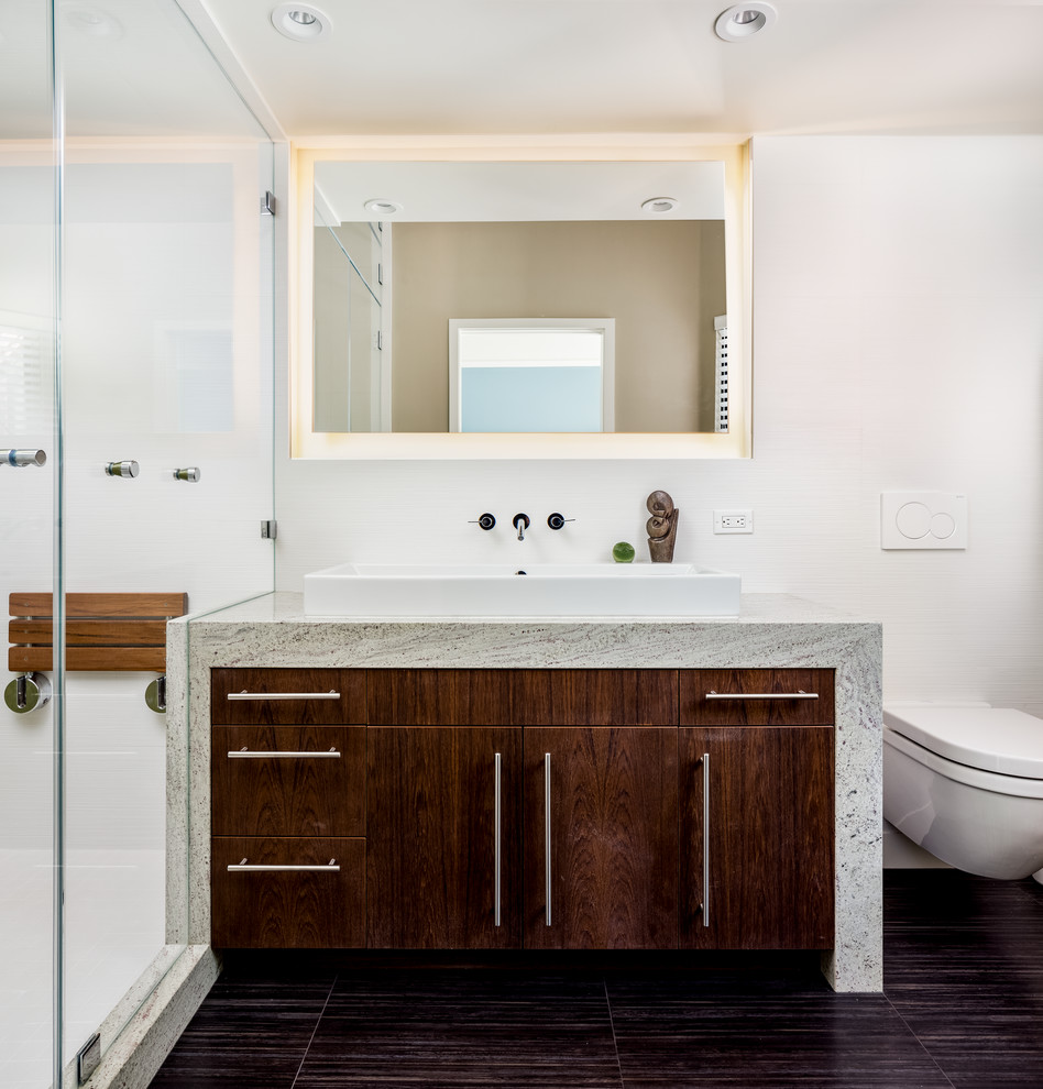 Bild på ett mellanstort funkis en-suite badrum, med ett fristående handfat, släta luckor, skåp i mörkt trä, granitbänkskiva, en dusch i en alkov, en vägghängd toalettstol, vit kakel, porslinskakel, vita väggar och klinkergolv i porslin