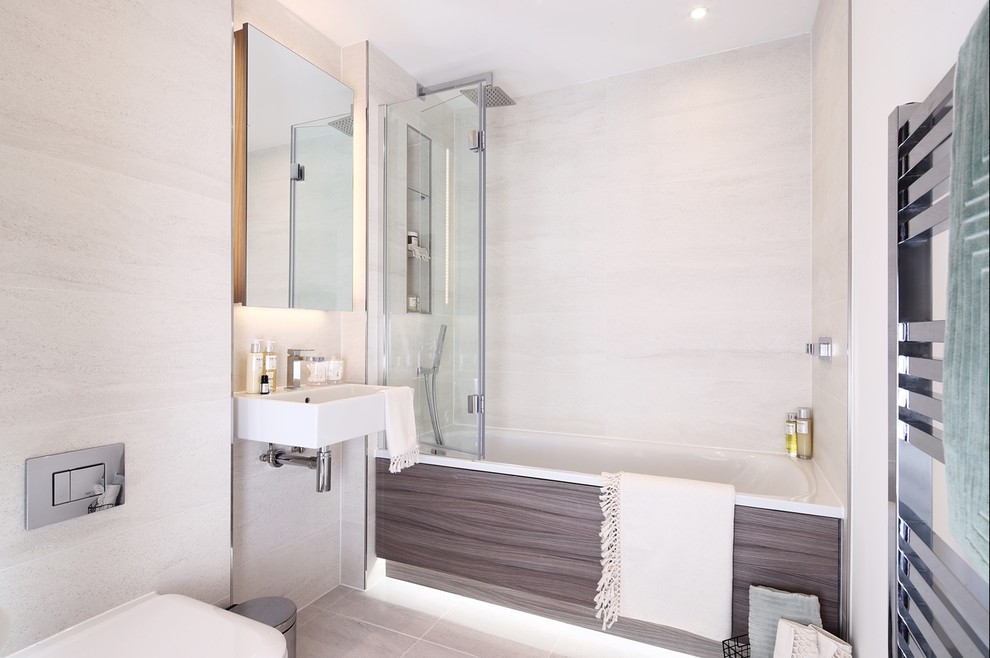 Modern inredning av ett mellanstort vit vitt en-suite badrum, med möbel-liknande, vita skåp, ett platsbyggt badkar, en dusch/badkar-kombination, en toalettstol med hel cisternkåpa, beige kakel, porslinskakel, beige väggar, klinkergolv i porslin, ett väggmonterat handfat, bänkskiva i rostfritt stål, beiget golv och med dusch som är öppen