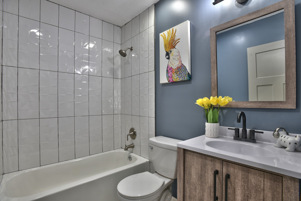 Modelo de cuarto de baño único tradicional renovado con armarios con paneles lisos, puertas de armario de madera oscura, bañera empotrada, combinación de ducha y bañera, baldosas y/o azulejos blancos, paredes azules, lavabo integrado y encimeras blancas