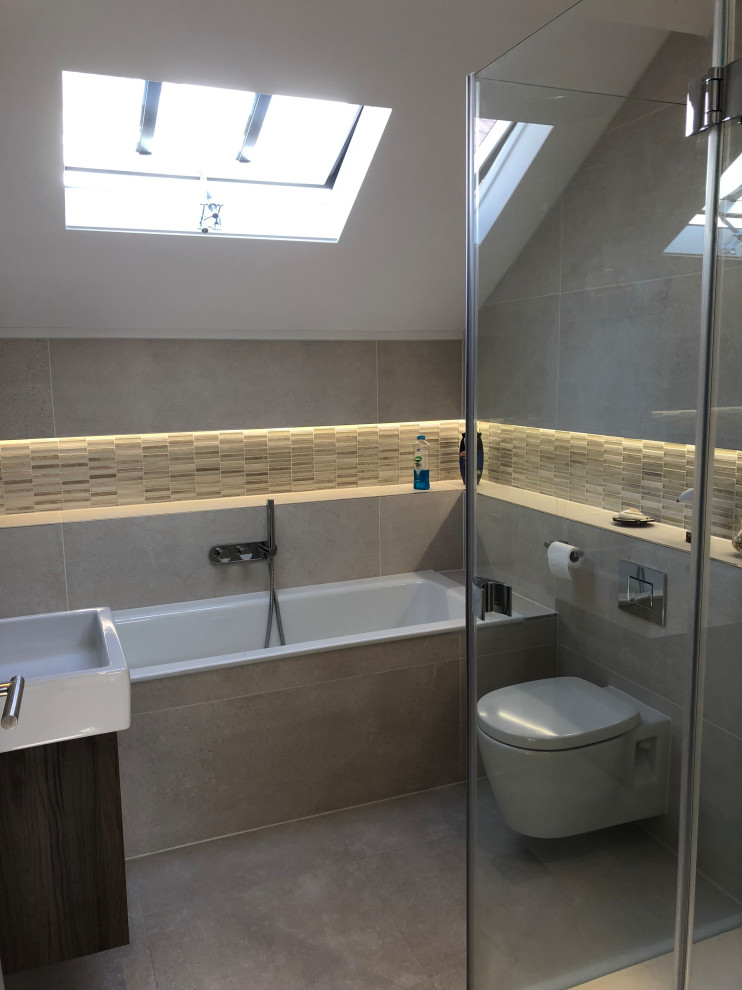 Small contemporary ensuite bathroom in Surrey with a wall mounted toilet, beige tiles, stone slabs, beige walls, porcelain flooring, a built-in sink, tiled worktops, brown floors, an open shower, beige worktops, a single sink and a built in vanity unit.