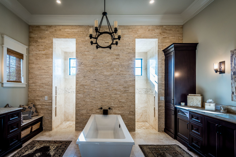Inspiration for a large rustic ensuite bathroom in Charleston with recessed-panel cabinets, dark wood cabinets, a freestanding bath, a walk-in shower, beige tiles, travertine tiles, beige walls, travertine flooring, a submerged sink, limestone worktops, beige floors, an open shower and a two-piece toilet.