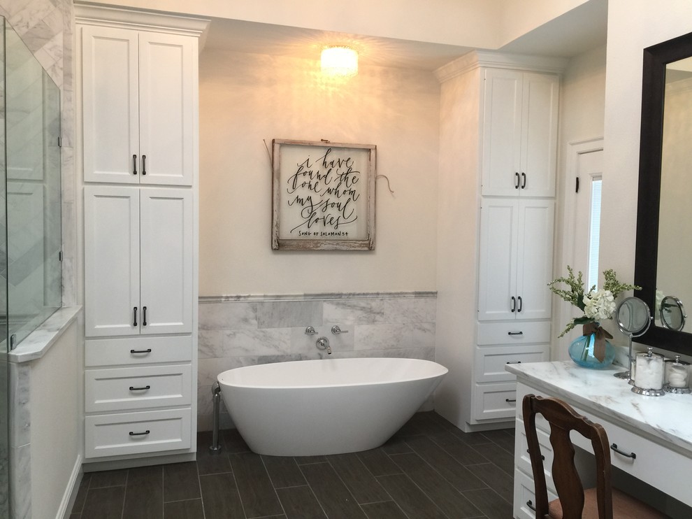 Large contemporary ensuite bathroom in Dallas with recessed-panel cabinets, white cabinets, a freestanding bath, a corner shower, a two-piece toilet, grey tiles, marble tiles, beige walls, porcelain flooring, a submerged sink, marble worktops, brown floors and a hinged door.