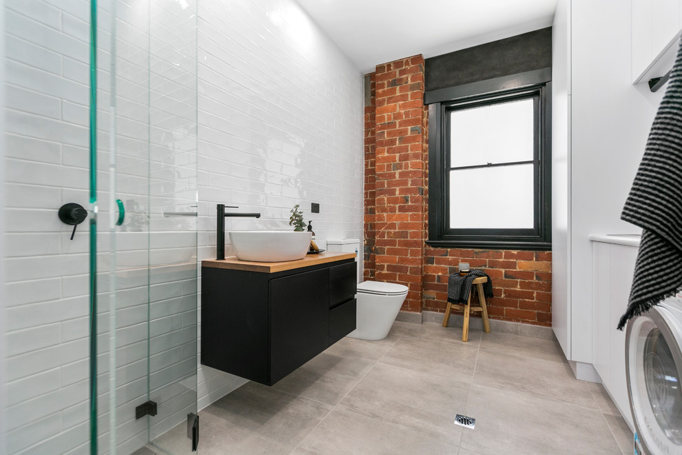 Trendy 3/4 white tile and subway tile gray floor bathroom/laundry room photo in Hobart with flat-panel cabinets, black cabinets, white walls, a vessel sink and wood countertops