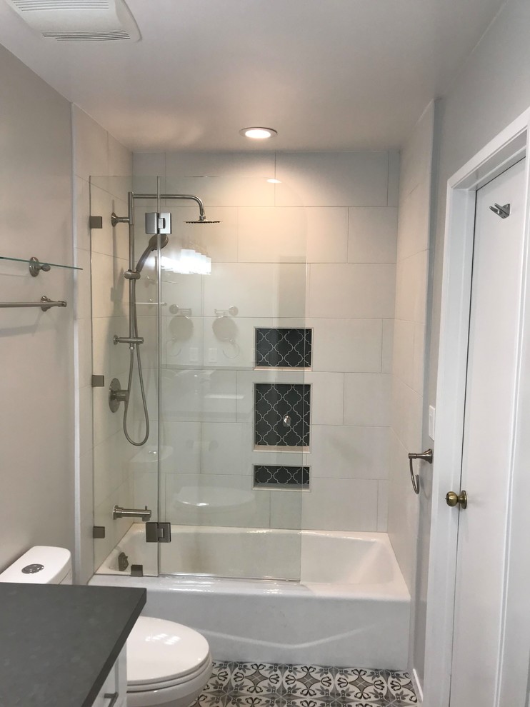 Example of a mid-sized classic master white tile and porcelain tile ceramic tile, multicolored floor and single-sink bathroom design in Los Angeles with recessed-panel cabinets, white cabinets, a one-piece toilet, white walls, an undermount sink, quartzite countertops, a hinged shower door, black countertops, a niche and a built-in vanity