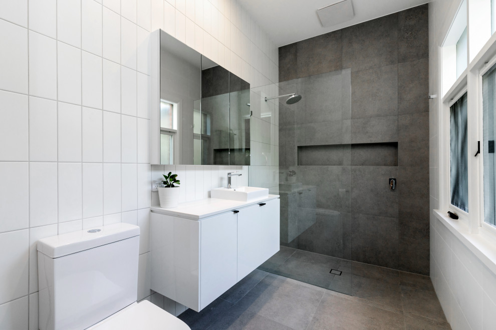 Inredning av ett modernt vit vitt badrum med dusch, med släta luckor, vita skåp, en kantlös dusch, en toalettstol med separat cisternkåpa, grå kakel, vita väggar, betonggolv, ett fristående handfat, grått golv och med dusch som är öppen