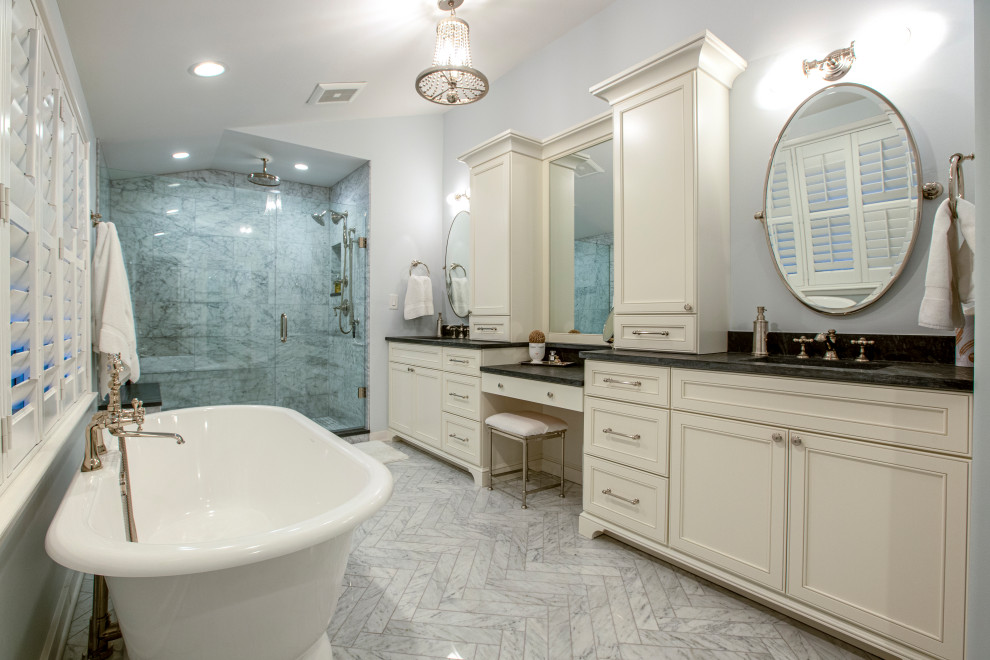 Photo of a medium sized traditional ensuite bathroom in Columbus with a freestanding bath, an alcove shower, marble tiles, grey walls, marble flooring, a submerged sink, a hinged door, black worktops, a shower bench, double sinks, a built in vanity unit, a vaulted ceiling, recessed-panel cabinets, beige cabinets, grey tiles and grey floors.