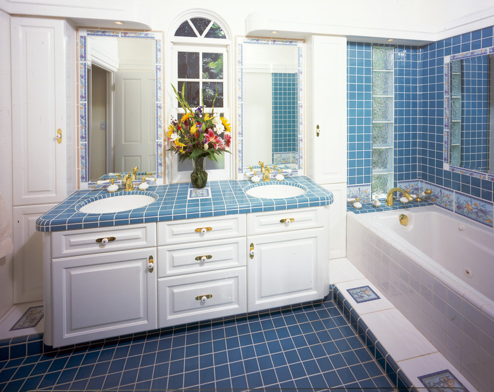 Imagen de cuarto de baño principal tradicional grande con lavabo bajoencimera, armarios con paneles lisos, puertas de armario blancas, encimera de azulejos, bañera esquinera, baldosas y/o azulejos azules y paredes blancas