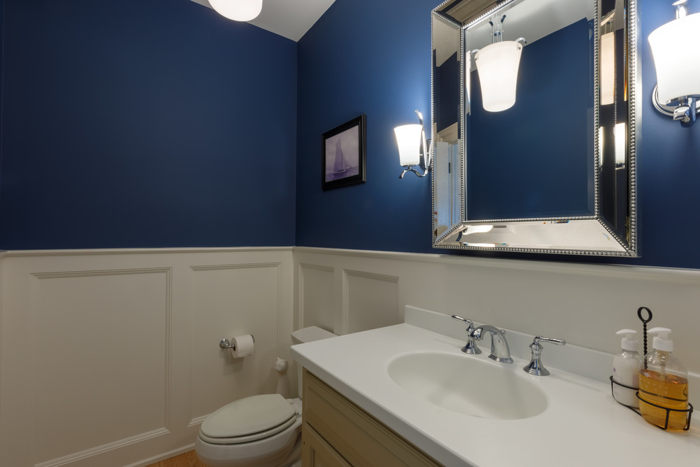 Réalisation d'une petite salle de bain tradition avec un placard avec porte à panneau surélevé, des portes de placard marrons, un mur bleu, un sol en bois brun, un plan vasque, un plan de toilette en surface solide et un plan de toilette blanc.