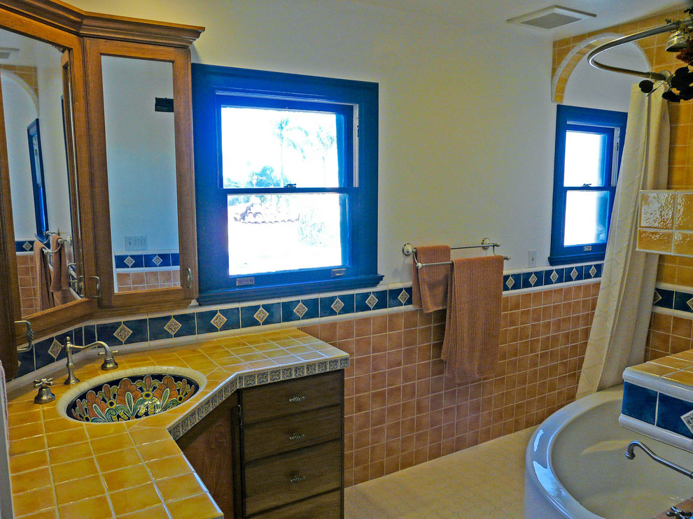 Bild på ett mellanstort amerikanskt en-suite badrum, med möbel-liknande, skåp i mörkt trä, ett hörnbadkar, en dusch/badkar-kombination, en toalettstol med hel cisternkåpa, gul kakel, keramikplattor, grå väggar, klinkergolv i keramik, ett undermonterad handfat och kaklad bänkskiva