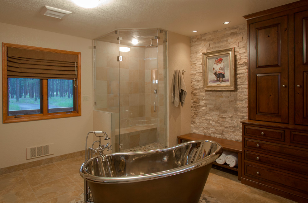 This is an example of a large rural ensuite bathroom in Albuquerque with raised-panel cabinets, dark wood cabinets, a claw-foot bath, a corner shower, beige tiles, stone tiles, beige walls, ceramic flooring, a vessel sink, solid surface worktops, beige floors and a hinged door.