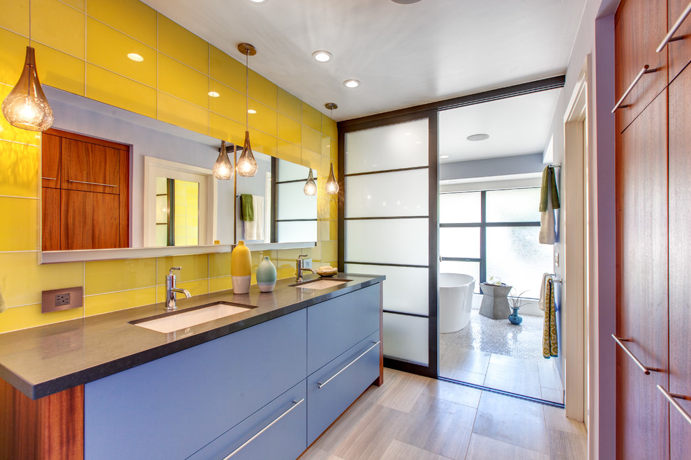 Foto de cuarto de baño principal actual con lavabo bajoencimera, armarios con paneles lisos, puertas de armario azules, bañera exenta y baldosas y/o azulejos amarillos