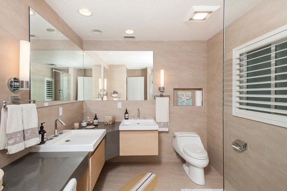 Inspiration for a large contemporary ensuite bathroom in Tampa with flat-panel cabinets, light wood cabinets, a one-piece toilet, beige tiles, porcelain tiles, beige walls, porcelain flooring, a vessel sink, beige floors, a corner shower and a hinged door.