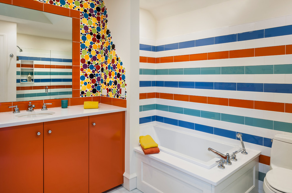 Diseño de cuarto de baño infantil ecléctico con armarios con paneles lisos, puertas de armario naranjas, sanitario de una pieza, baldosas y/o azulejos multicolor, baldosas y/o azulejos azules, baldosas y/o azulejos naranja, baldosas y/o azulejos blancos, baldosas y/o azulejos de cerámica, lavabo bajoencimera y bañera encastrada