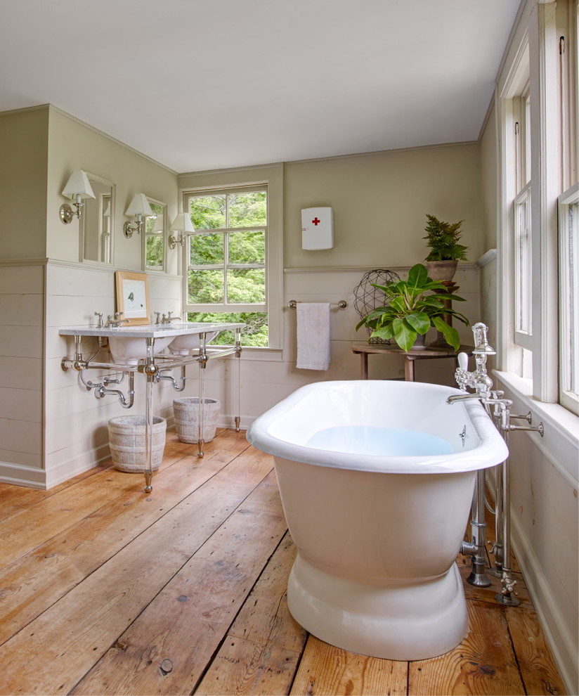 Aménagement d'une salle de bain campagne avec une baignoire indépendante, un mur vert, un sol en bois brun et un lavabo de ferme.