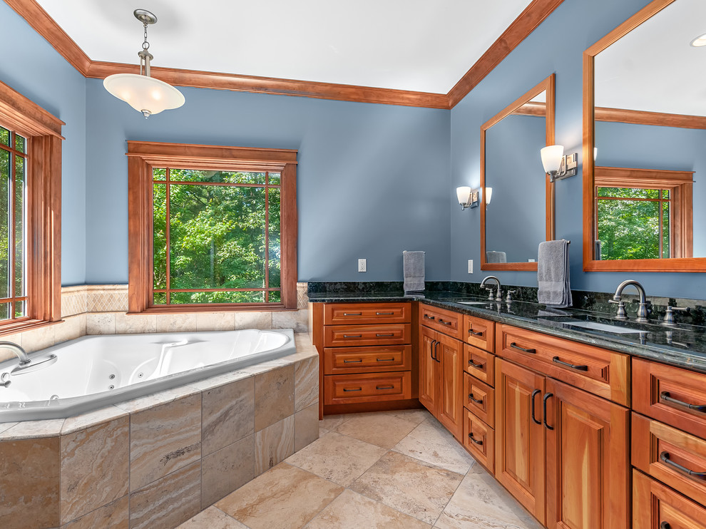 Aménagement d'une salle de bain principale craftsman en bois brun de taille moyenne avec un placard avec porte à panneau surélevé, une baignoire d'angle, un carrelage beige, un mur bleu, un sol en carrelage de porcelaine, un lavabo encastré, un plan de toilette en granite, un sol beige et un plan de toilette noir.
