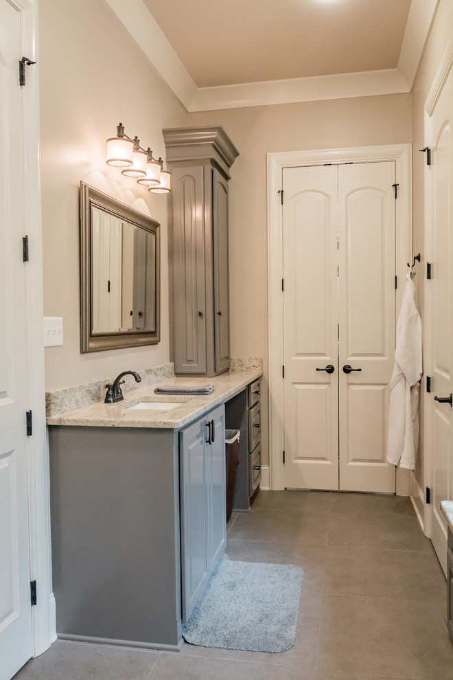Réalisation d'une salle de bain tradition de taille moyenne avec un placard avec porte à panneau surélevé, des portes de placard grises, un mur beige, un sol en carrelage de porcelaine, un lavabo encastré et un sol marron.