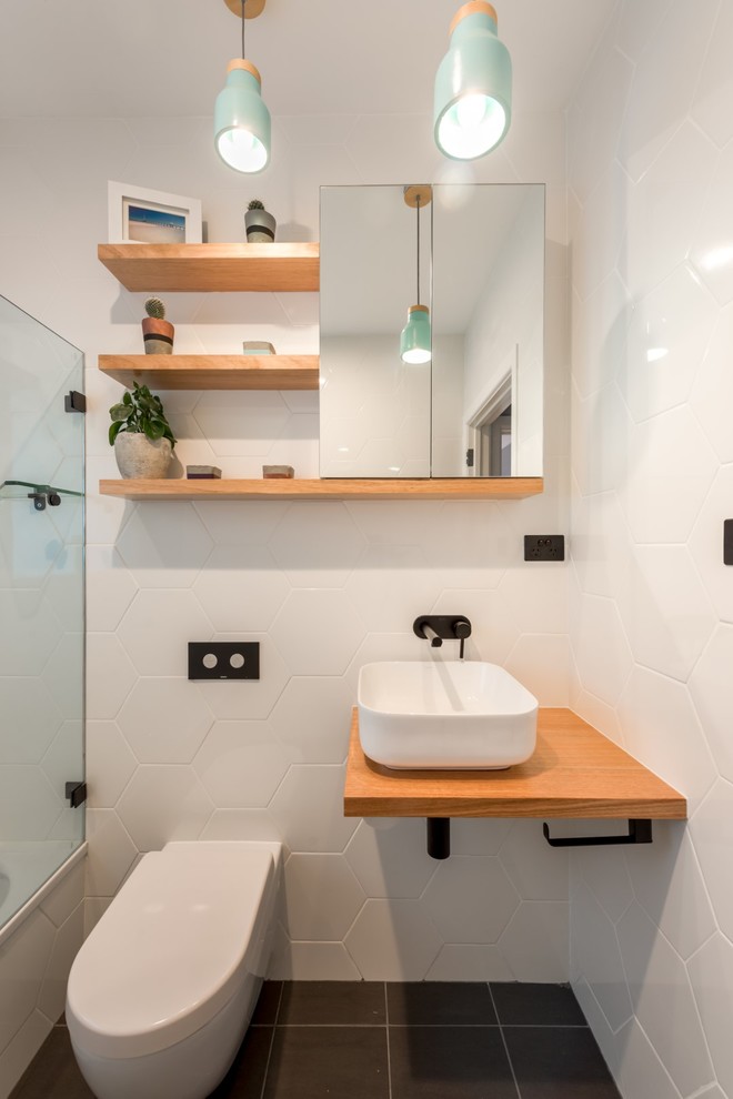 Foto på ett litet funkis badrum med dusch, med öppna hyllor, vita skåp, en dusch/badkar-kombination, en vägghängd toalettstol, vit kakel, keramikplattor, klinkergolv i porslin, ett fristående handfat, träbänkskiva och grått golv