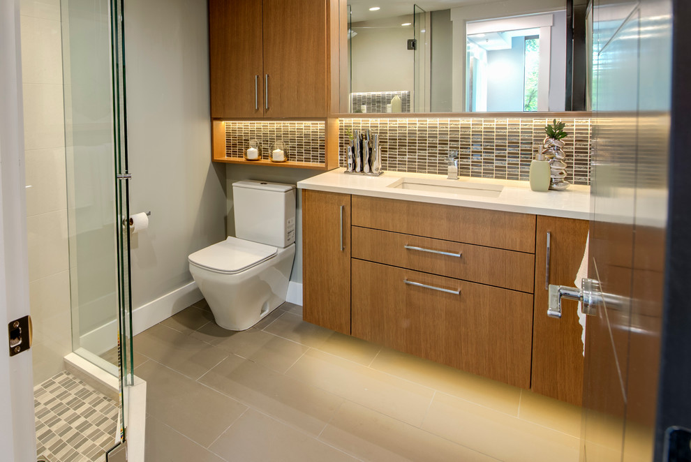 Photo of a small traditional shower room bathroom in Vancouver with flat-panel cabinets, medium wood cabinets, a corner shower, a two-piece toilet, multi-coloured tiles, glass tiles, blue walls, ceramic flooring, a submerged sink and quartz worktops.