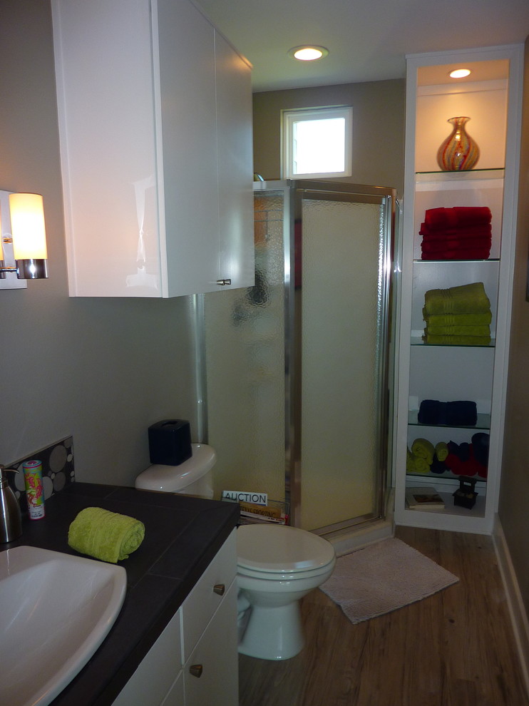 Inspiration för små moderna en-suite badrum, med släta luckor, vita skåp, en hörndusch, en toalettstol med separat cisternkåpa, grå kakel, grå väggar, ljust trägolv och ett nedsänkt handfat