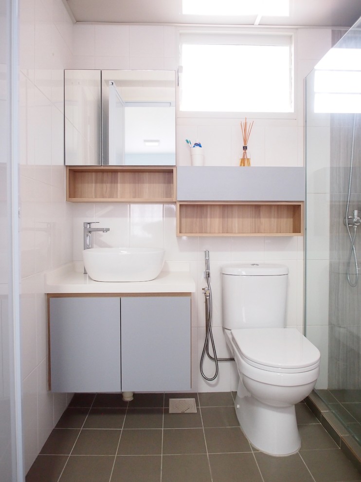 Bild på ett funkis vit vitt badrum med dusch, med släta luckor, grå skåp, en hörndusch, vit kakel, vita väggar, ett fristående handfat och grått golv