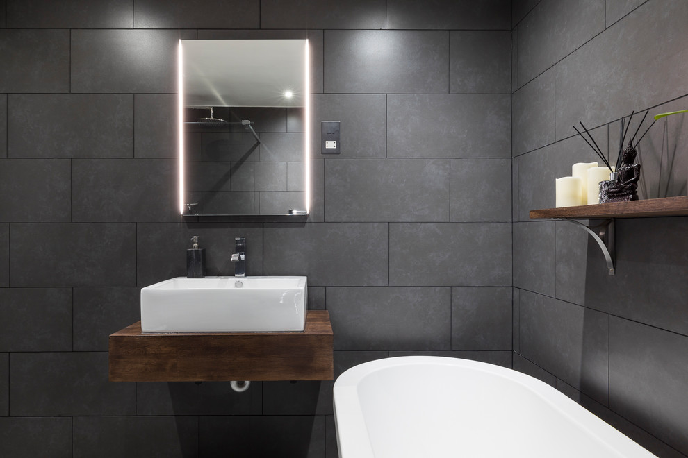 Photo of a large modern family bathroom in London with raised-panel cabinets, dark wood cabinets, a freestanding bath, a shower/bath combination, a one-piece toilet, grey tiles, cement tiles, grey walls, ceramic flooring, a pedestal sink and wooden worktops.