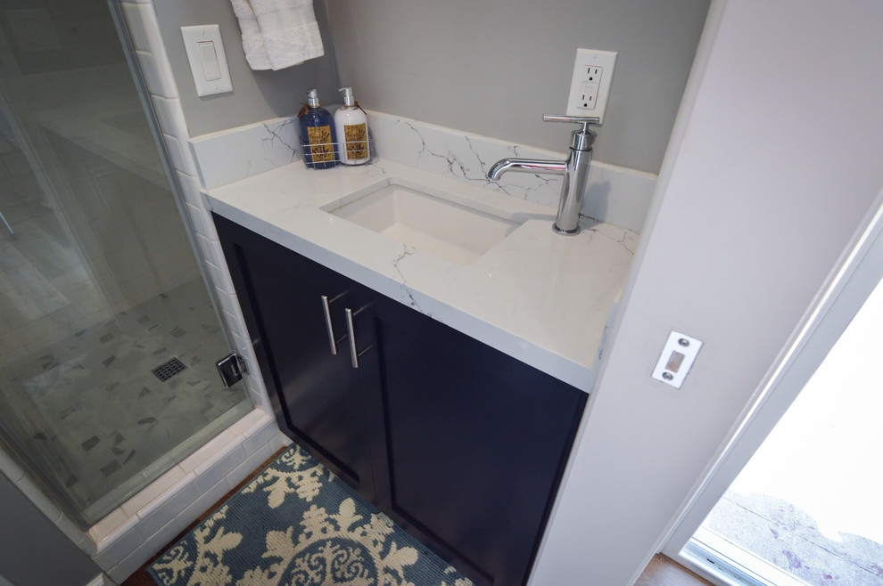 Example of a small trendy 3/4 white tile and porcelain tile laminate floor and brown floor corner shower design in Los Angeles with shaker cabinets, blue cabinets, a two-piece toilet, gray walls, an undermount sink, quartz countertops, a hinged shower door and white countertops