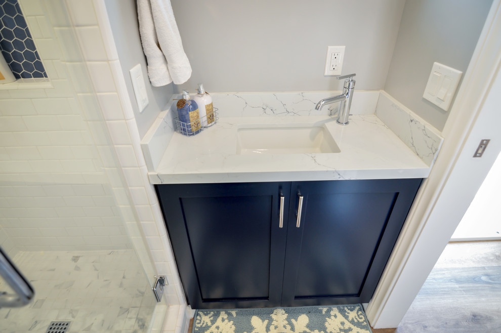 Стильный дизайн: маленькая ванная комната в современном стиле с фасадами в стиле шейкер, синими фасадами, угловым душем, раздельным унитазом, белой плиткой, керамогранитной плиткой, серыми стенами, полом из ламината, душевой кабиной, врезной раковиной, столешницей из искусственного кварца, коричневым полом, душем с распашными дверями и белой столешницей для на участке и в саду - последний тренд