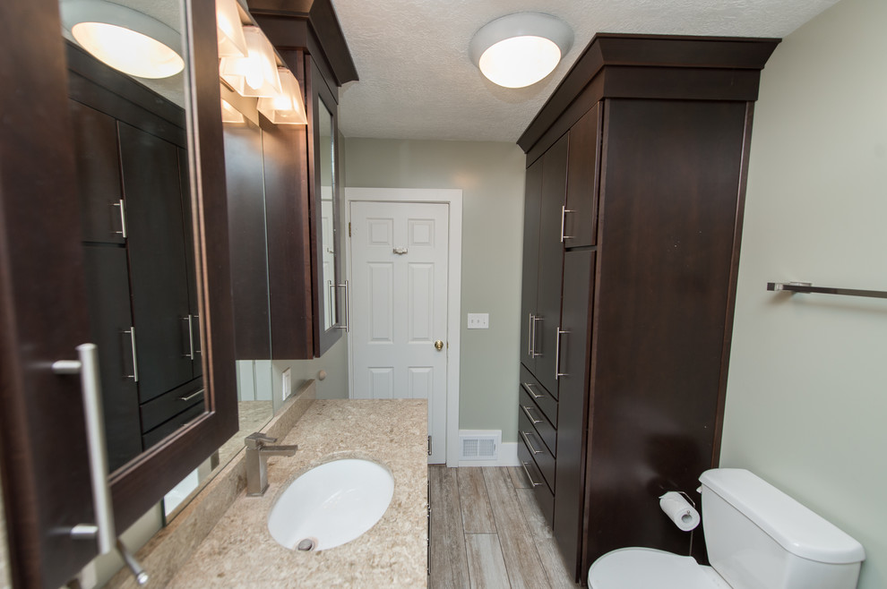 Example of a mid-sized transitional 3/4 porcelain tile and brown floor bathroom design in Other with flat-panel cabinets, brown cabinets, a two-piece toilet, green walls, an undermount sink and quartz countertops