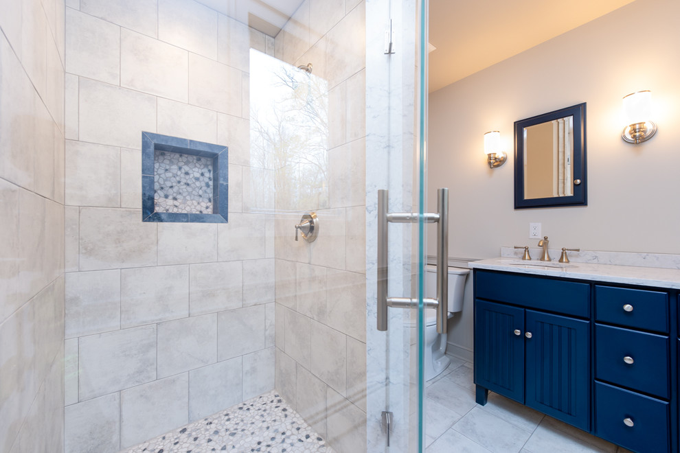 Стильный дизайн: ванная комната в стиле неоклассика (современная классика) с фасадами с декоративным кантом, синими фасадами, душем в нише, раздельным унитазом, серой плиткой, керамогранитной плиткой, бежевыми стенами, полом из галечной плитки, врезной раковиной, столешницей из искусственного кварца, серым полом, душем с распашными дверями и серой столешницей - последний тренд