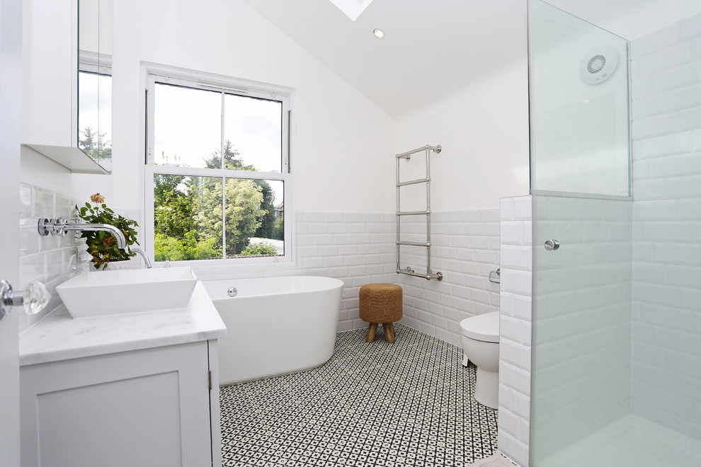 Пример оригинального дизайна: ванная комната среднего размера в современном стиле с фасадами с выступающей филенкой, белыми фасадами, отдельно стоящей ванной, открытым душем, унитазом-моноблоком, плиткой кабанчик, белыми стенами, полом из керамической плитки, настольной раковиной, мраморной столешницей, разноцветным полом и душем с распашными дверями