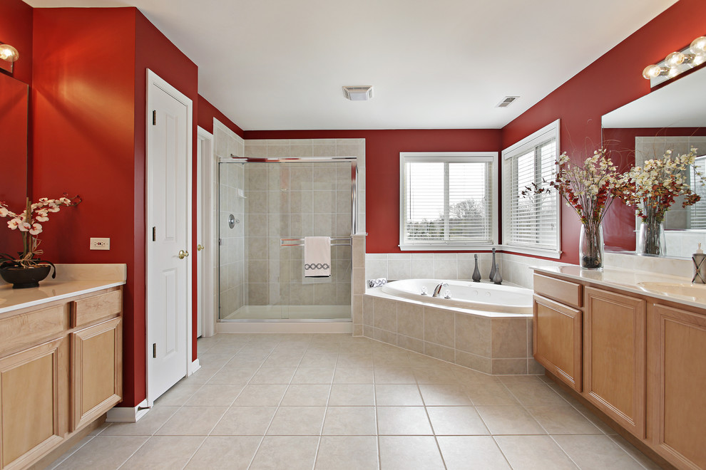 Aménagement d'une grande salle de bain classique en bois clair avec un placard avec porte à panneau surélevé, un plan de toilette en surface solide, une baignoire d'angle, un carrelage beige, des carreaux de porcelaine, un mur rouge, un sol en carrelage de porcelaine et un lavabo encastré.