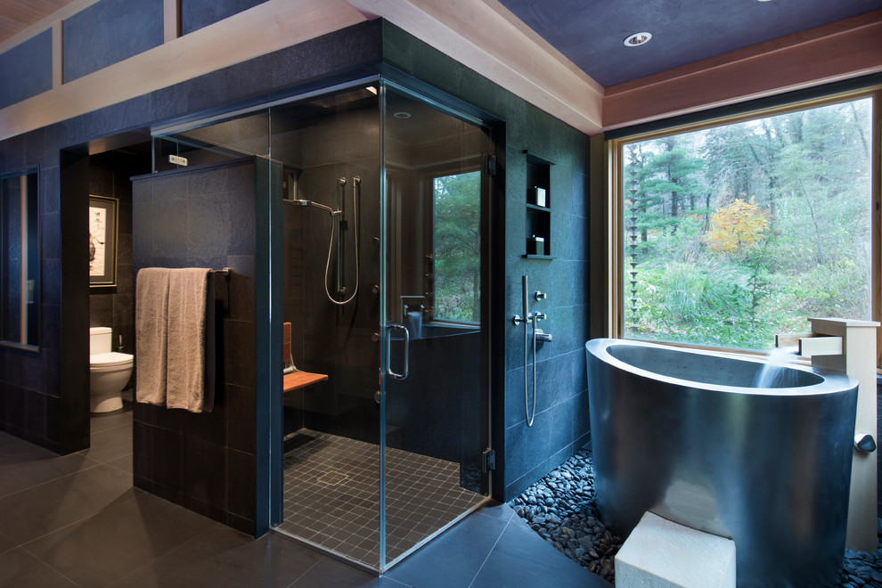 Idéer för ett stort asiatiskt en-suite badrum, med ett japanskt badkar, en kantlös dusch, en toalettstol med hel cisternkåpa, grå kakel, stenkakel, grå väggar, luckor med lamellpanel, skåp i ljust trä, klinkergolv i porslin, ett undermonterad handfat, granitbänkskiva, svart golv och med dusch som är öppen