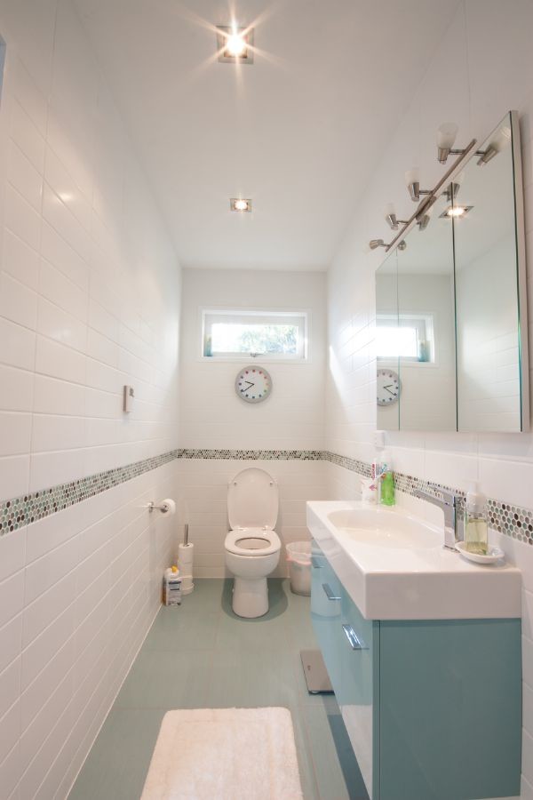 オークランドにある小さなコンテンポラリースタイルのおしゃれなバスルーム (浴槽なし) (フラットパネル扉のキャビネット、青いキャビネット、一体型トイレ	、白いタイル、セラミックタイル、白い壁、セラミックタイルの床、一体型シンク、人工大理石カウンター、緑の床) の写真