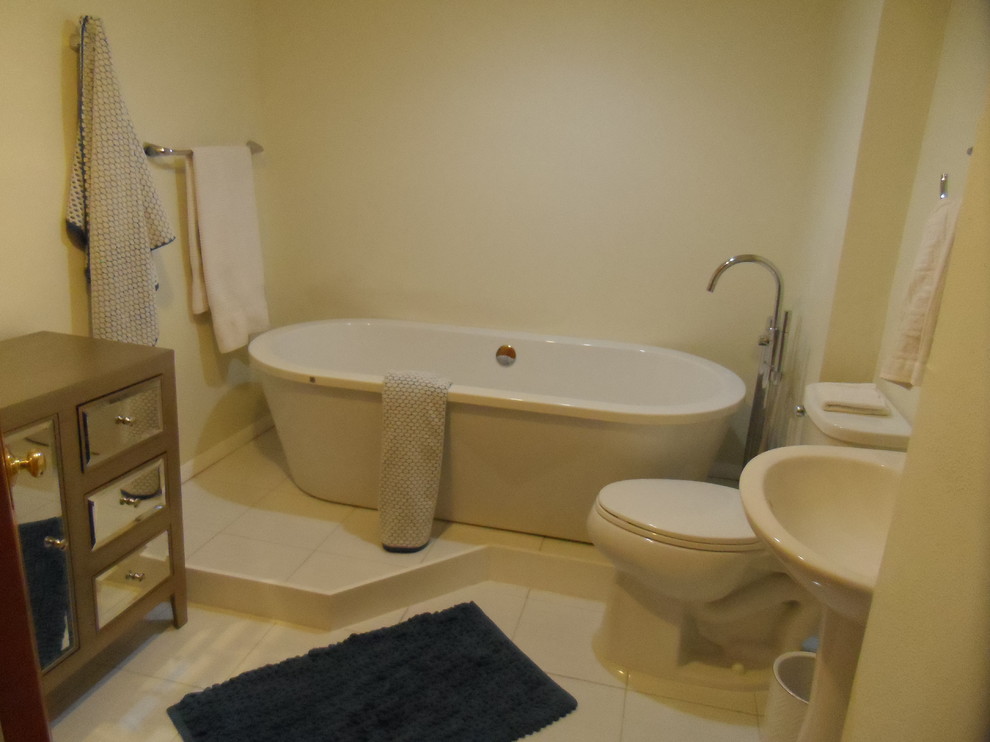 Inredning av ett 50 tals mellanstort badrum, med ett piedestal handfat, ett fristående badkar, en toalettstol med hel cisternkåpa, beige kakel, porslinskakel, beige väggar och klinkergolv i porslin