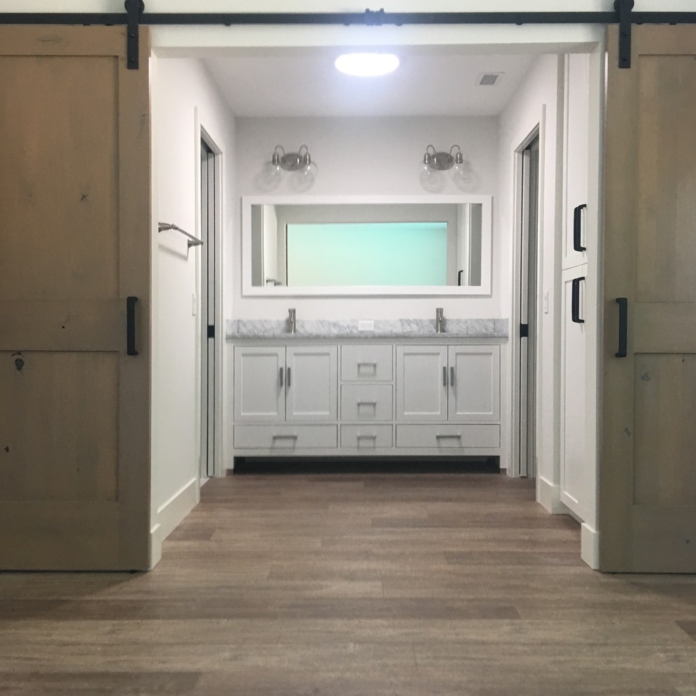 Пример оригинального дизайна: главная ванная комната среднего размера в стиле ретро с фасадами в стиле шейкер, белыми фасадами, душем в нише, унитазом-моноблоком, белой плиткой, плиткой кабанчик, серыми стенами, полом из ламината, врезной раковиной, мраморной столешницей, коричневым полом и душем с распашными дверями