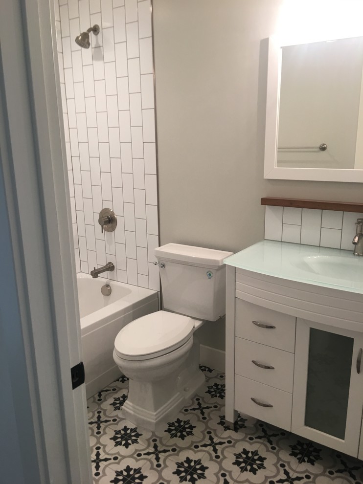 Пример оригинального дизайна: маленькая детская ванная комната в стиле ретро с плоскими фасадами, белыми фасадами, душем над ванной, белой плиткой, плиткой кабанчик, серыми стенами, полом из цементной плитки, монолитной раковиной, стеклянной столешницей, разноцветным полом, шторкой для ванной, ванной в нише и раздельным унитазом для на участке и в саду