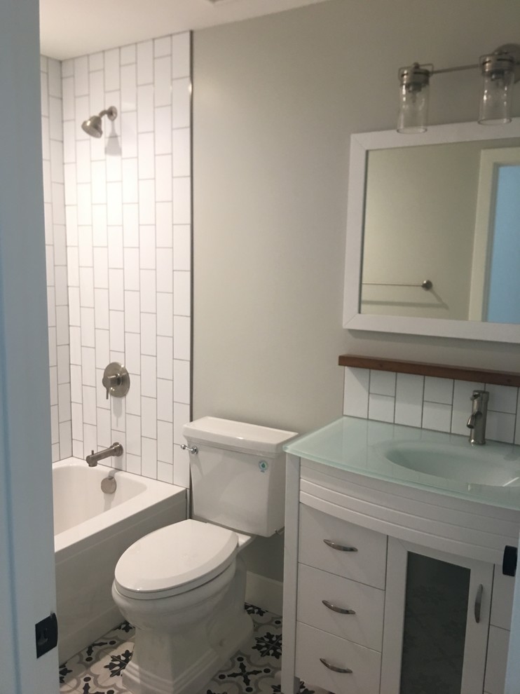 На фото: маленькая детская ванная комната в стиле ретро с плоскими фасадами, белыми фасадами, накладной ванной, душем над ванной, унитазом-моноблоком, белой плиткой, плиткой кабанчик, серыми стенами, полом из цементной плитки, монолитной раковиной, стеклянной столешницей, разноцветным полом и шторкой для ванной для на участке и в саду