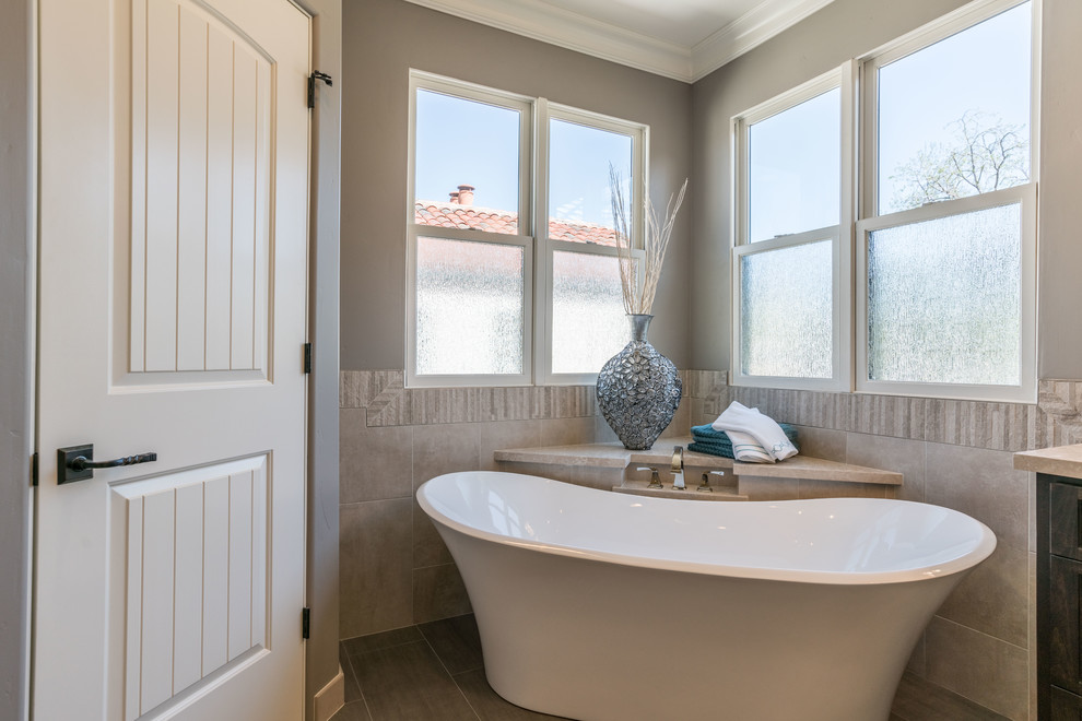 Photo of a medium sized ensuite bathroom in San Francisco with dark wood cabinets, a freestanding bath, a one-piece toilet, beige tiles, stone tiles, brown walls, porcelain flooring, a submerged sink, limestone worktops, brown floors and beige worktops.