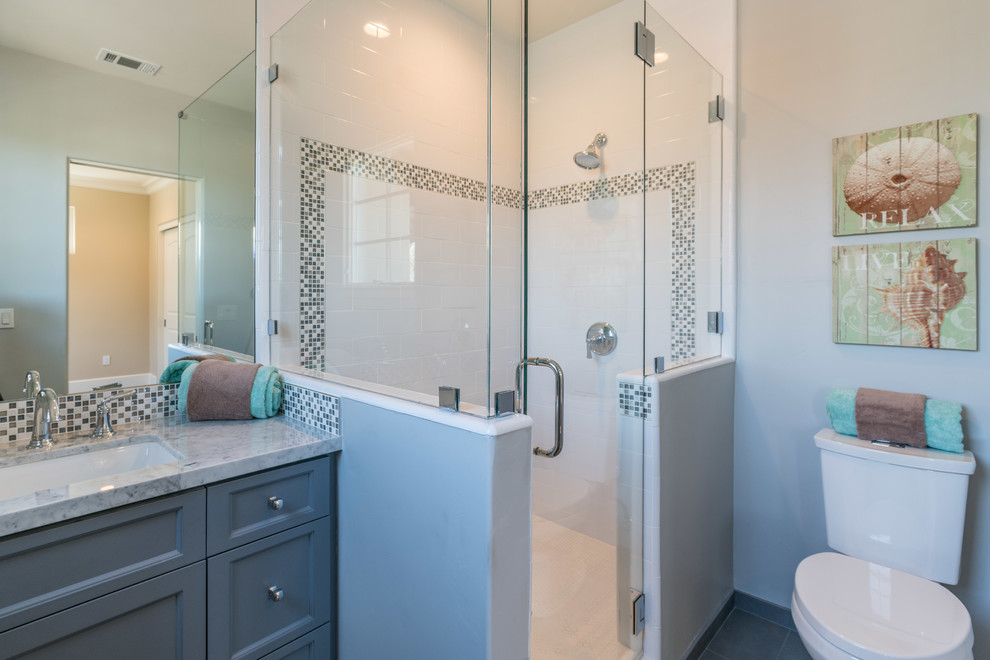 This is an example of a medium sized nautical ensuite bathroom in San Francisco with recessed-panel cabinets, grey cabinets, a corner shower, a two-piece toilet, white tiles, ceramic tiles, grey walls, porcelain flooring, a submerged sink, marble worktops, grey floors, a hinged door and grey worktops.