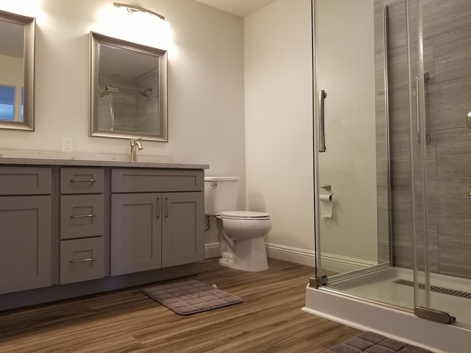 Foto på ett mellanstort vintage grå badrum med dusch, med skåp i shakerstil, bruna skåp, en hörndusch, en toalettstol med separat cisternkåpa, grå kakel, porslinskakel, vita väggar, mellanmörkt trägolv, ett undermonterad handfat, granitbänkskiva, brunt golv och dusch med skjutdörr