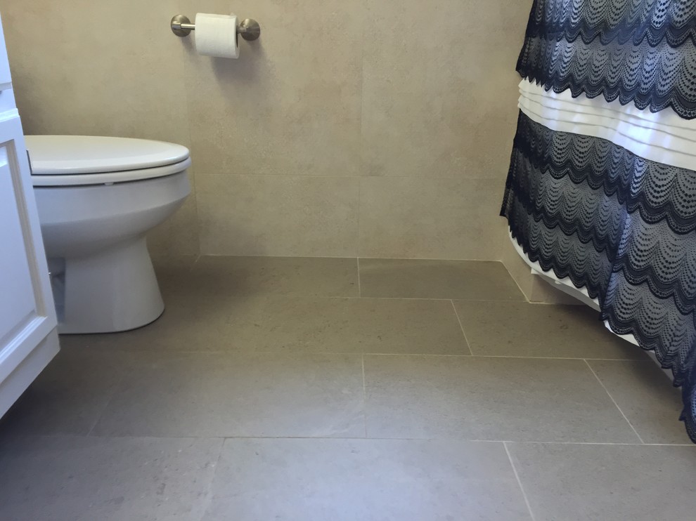 Inredning av ett badrum, med ett undermonterad handfat, vita skåp, bänkskiva i kvarts, ett badkar i en alkov, en dusch i en alkov, en toalettstol med separat cisternkåpa, beige kakel, porslinskakel, beige väggar och klinkergolv i porslin