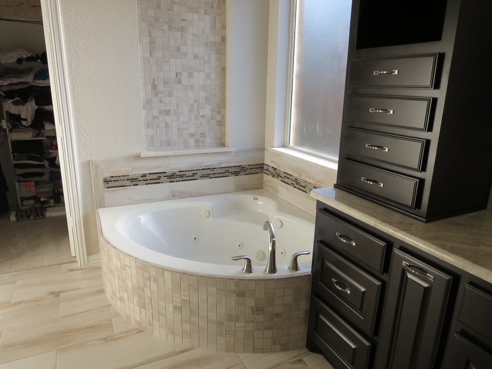 Exemple d'une grande salle de bain principale chic avec un placard avec porte à panneau surélevé, des portes de placard noires, une baignoire d'angle, une douche d'angle, un carrelage beige, des carreaux de porcelaine, un mur blanc, un sol en carrelage de porcelaine, un plan de toilette en surface solide et un lavabo encastré.