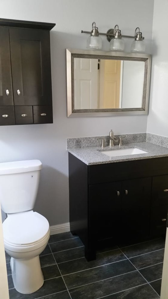 Inredning av ett klassiskt mellanstort badrum med dusch, med skåp i shakerstil, svarta skåp, en toalettstol med separat cisternkåpa, grå väggar, klinkergolv i porslin, ett undermonterad handfat, granitbänkskiva och svart golv