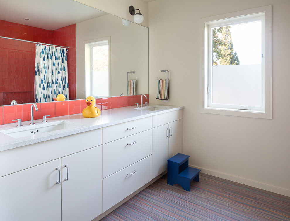 Exemple d'une salle de bain moderne de taille moyenne pour enfant avec un placard à porte plane, des portes de placard blanches, un combiné douche/baignoire, un carrelage orange, des carreaux de porcelaine, un mur blanc, un sol en linoléum, un lavabo encastré, un plan de toilette en verre recyclé et un sol multicolore.