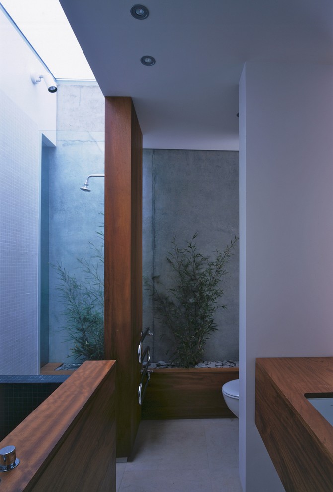 Inspiration for a medium sized modern ensuite bathroom in London with a submerged sink, flat-panel cabinets, medium wood cabinets, wooden worktops, a shower/bath combination, a wall mounted toilet, white tiles, stone tiles, grey walls and limestone flooring.