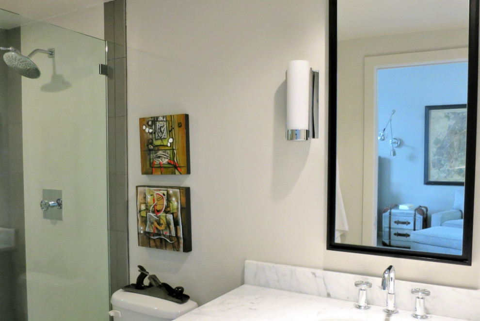 Small urban ensuite bathroom in Houston with flat-panel cabinets, black cabinets, an alcove shower, a two-piece toilet, white tiles, porcelain tiles, white walls, porcelain flooring, marble worktops, white floors, a hinged door, white worktops, a single sink, a freestanding vanity unit, a submerged sink and brick walls.