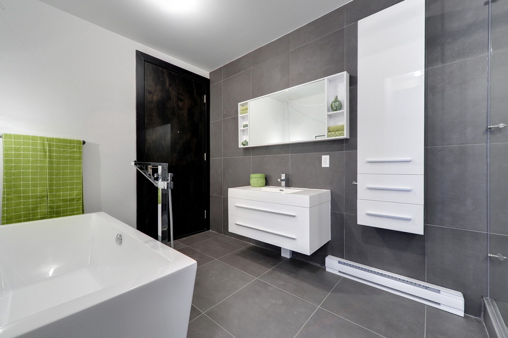 This is an example of a contemporary grey and white bathroom in Montreal with flat-panel cabinets, white cabinets, a freestanding bath, grey tiles and grey floors.