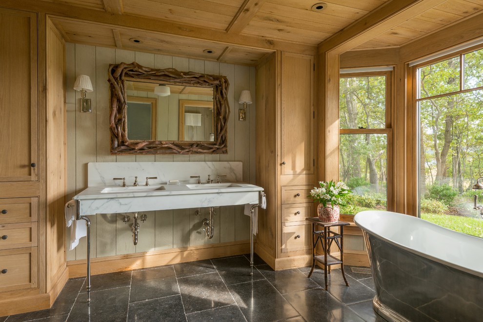 Freestanding bathtub - large rustic master ceramic tile and black floor freestanding bathtub idea in New York with shaker cabinets, light wood cabinets, brown walls, marble countertops and a console sink