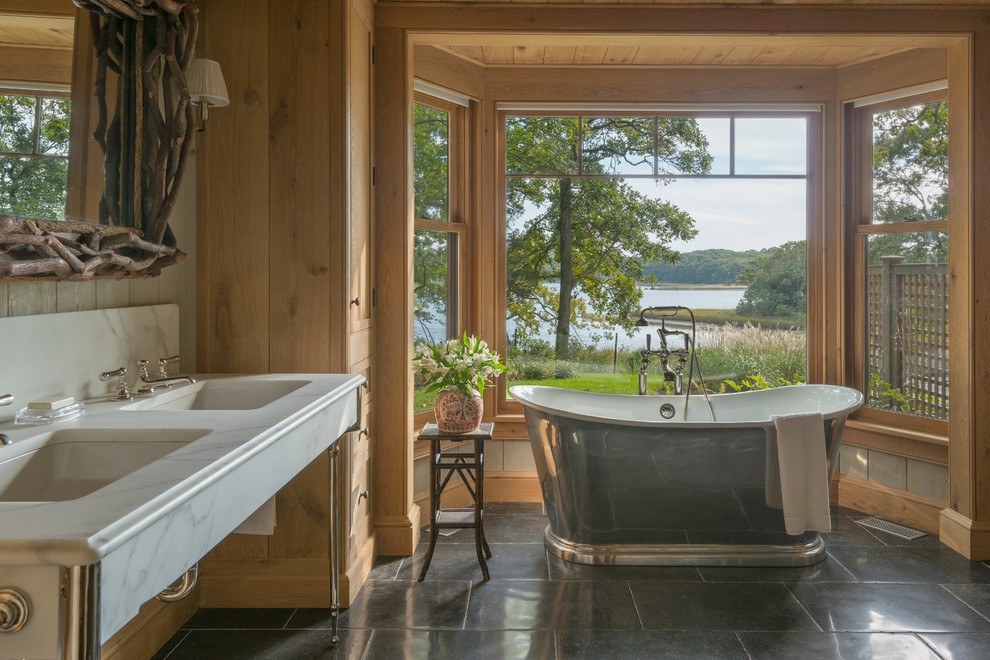 Idées déco pour une grande salle de bain principale montagne en bois clair avec un placard à porte shaker, une baignoire indépendante, un mur marron, un sol en carrelage de céramique, un lavabo de ferme, un plan de toilette en marbre et un sol noir.