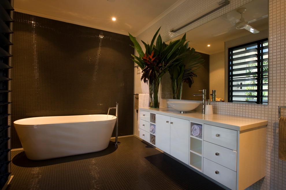 Bathroom - large tropical master black tile and mosaic tile mosaic tile floor bathroom idea in Darwin with a vessel sink, flat-panel cabinets, white cabinets, solid surface countertops, a one-piece toilet and white walls